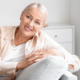 Frau mit heller Kleidung sitzt auf einem Sofa und zeigt Ihre weißen Zähne in den Wechseljahren