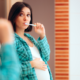 Schwangere Frau steht vor dem Spiegel und putzt sich die Zähne